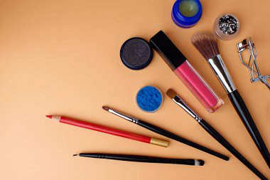 Dört makyaj fırçası, allık için fırça, göz farı, ruj, göz farı, pembe ruj, dudak parlatıcısı ve kırmızı dudak kalemi. Randevuya hazır ol. Uzayı kopyala Şeftali arkaplan.