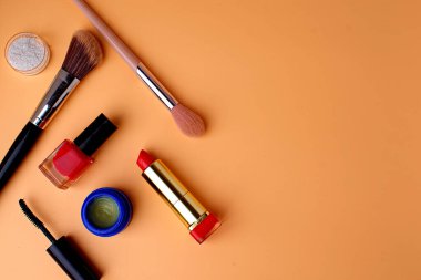 Makyaj fırçaları, dudak parlatıcısı, kırmızı ruj ve kırmızı oje. Şeftali arkaplan. Boşluğu kopyala.