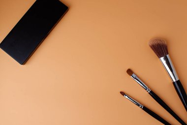 Üç makyaj fırçası, allık için fırça, göz farı, ruj ve göz farı paleti. Uzayı kopyala Şeftali arkaplan.