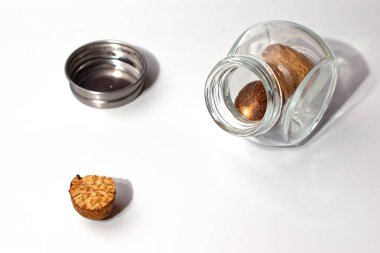 Hindistan cevizli küçük cam kavanoz, yanında metal kapaklar. Ön planda yarım fındık var. İzole et