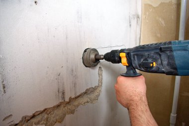 Prizi delmek için delgiyle delik açmak. Müteahhit için özel kıyafetler. Yakın plan. Elektrik tamiratı ve elektrik tesisatı konsepti.
