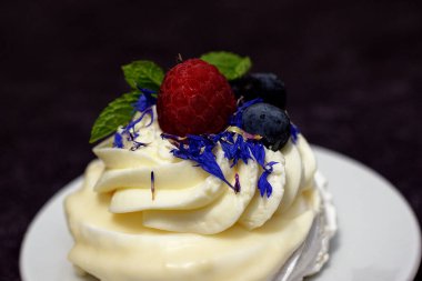 Madam Pavlova 'ya taze ahududu ve böğürtlenli nane ve mısır çiçeğiyle süslenmiş tatlı verin. Kremalı ve kremalı hafif tatlı..