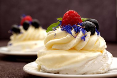 Madam Pavlova 'ya taze ahududu ve böğürtlenli nane ve mısır çiçeğiyle süslenmiş tatlı verin. Kremalı ve kremalı hafif tatlı. Macro, kapat..