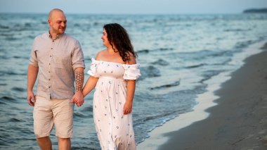 Bir çift kumlu bir plajda el ele yürür, dalgalar yavaşça ayaklarına vururken birbirlerine gülümserler. Gün sona ererken gökyüzü sıcacık renklerle parlar.