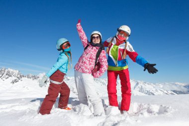Fransız Alplerinde kış tatilindeki üç genç kız karda ceketli ve kayak kasklı poz veriyorlar.