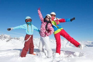 Kış tatilinde dağlarda kayak malzemeleriyle poz veren üç genç kız.