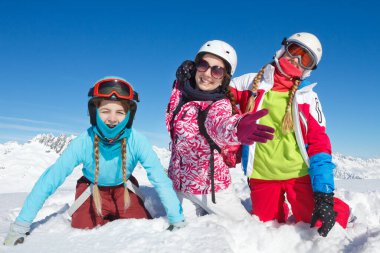 Fransa 'da kış tatilindeki mutlu çocuklar taze karda oynar ve kayak pistlerinde kamera önünde poz verir.