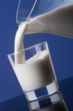 Sürahiden bardağa dökülen lezzetli kremalı taze süt mavi arka planda izole edilmiş.