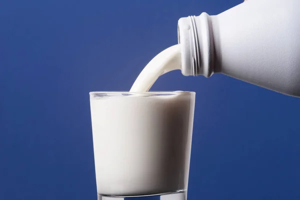 Пляшка Молока Вливається Склянку Краю Ізольована Синьому Фоні — стокове фото