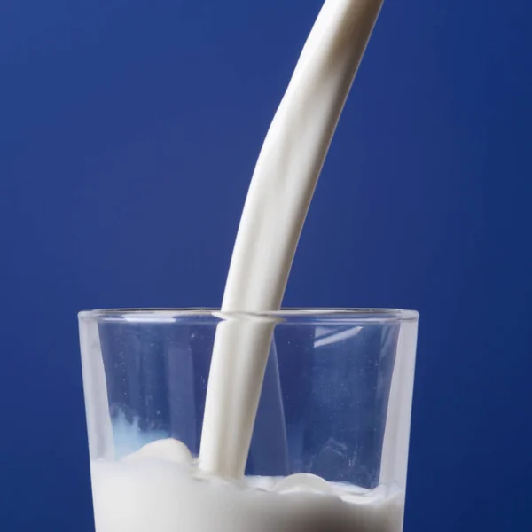 Крупним Планом Молоко Вливається Склянку Ізольовано Синьому Фоні — стокове фото