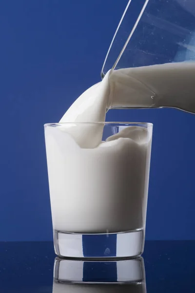 鲜奶油牛奶倒入玻璃瓶中 倒入玻璃瓶中 用蓝色衬底隔开 — 图库照片