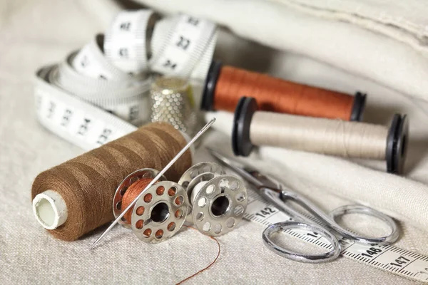 sewing tools with scissors, brown threads, needle and tape measure. Dressmakers accessories on beige fabrics