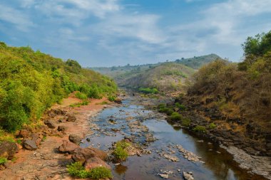 Mavi gökyüzü ile güzel bir manzara ve güneşli bir gün. Nehir, kayalık tepeler ve ormanla..