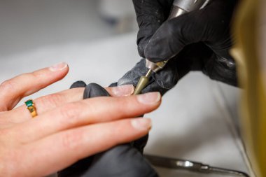 Güzellik stüdyosunda, usta donanım manikürü yapar. Jel cilasını kesiciyle çıkarıyorum. Parmaklardaki tırnak etlerini siler.