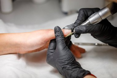 Güzellik stüdyosunda, usta donanım manikürü yapar. Jel cilasını kesiciyle sökmek