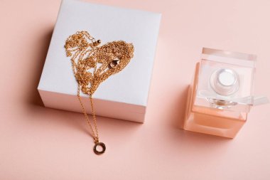 Sevgililer Günü hediyesi. Parfüm ve pembe arka planda altın zincirli bir kutu..