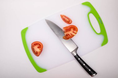Kesme tahtasının üzerinde taze kırmızı bir domates ve büyük bir şef bıçağı var. İzole edilmiş beyaz bir arkaplanda.