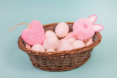 Paskalya. Üniformalı mavi arka planda yapay tavşanlı sepetteki beyaz yumurtalar. Metin için yer.