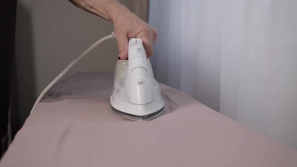 Un hombre planchando ropa de cama con una plancha eléctrica blanca en una tabla de planchar. — Vídeos de Stock