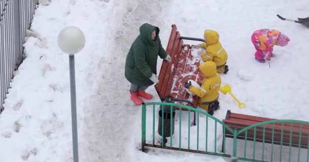 Niños en el patio esculpen una bola de nieve en el banco. — Vídeos de Stock