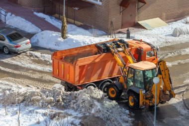 Mini bir traktör kar küreyerek bir kamyonun arkasına yükler..