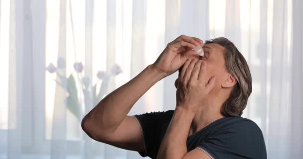 Un hombre de pelo gris adulto gotea gotas para los ojos. Ojos secos. — Vídeo de stock