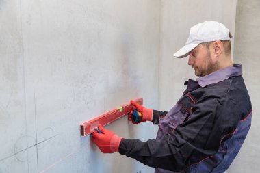 Bir adam, bir elektrikçi bir kalem ve mezura ile soketler için delikler açar.