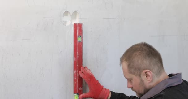A man, an electrician marks out holes for sockets with a pencil, a tape measure — Stock Video