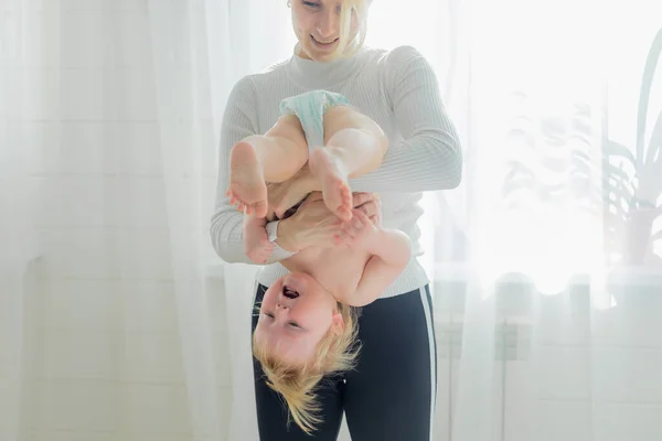 Mom holds the baby upside down, is engaged in childrens gymnastics.