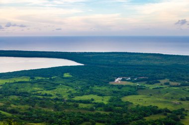 Dominik Cumhuriyeti 'nde gölü olan büyük bir dağdan vadiye manzara. Güneş batıyor. Yeşillik ve kırmızı çalıların etrafında