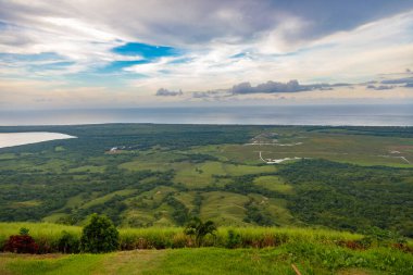 Dominik Cumhuriyeti 'nde gölü olan büyük bir dağdan vadiye manzara. Güneş batıyor. Yeşillik ve kırmızı çalıların etrafında