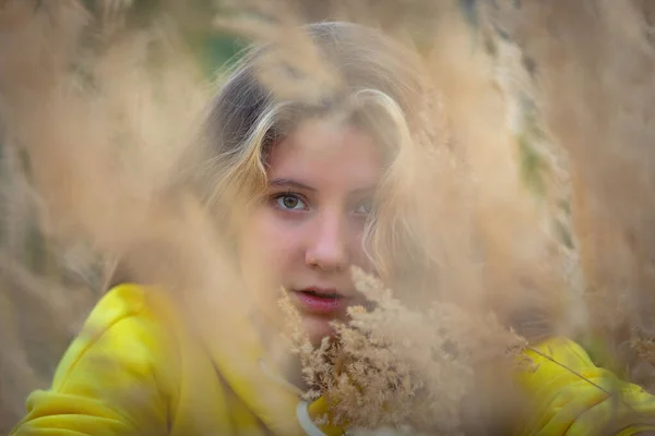 Ein junges Mädchen mit langen Haaren geht über ein Feld mit hohem Gras. Blonde Haare. — Stockfoto