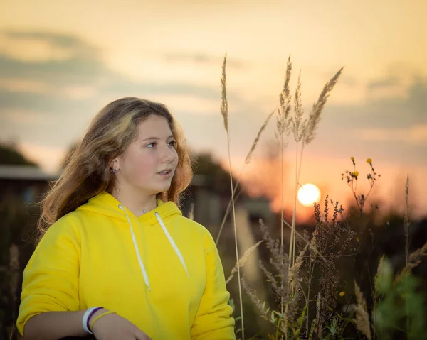 Ein junges Mädchen auf einer Wiese mit hohem Gras im Licht der untergehenden Sonne. — Stockfoto