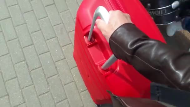 Чоловік катає велику червону валізу на тротуарі на колесах — стокове відео
