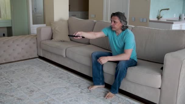 Dorosły mężczyzna ogląda telewizję, zmieniając kanały za pomocą pilota TV — Wideo stockowe