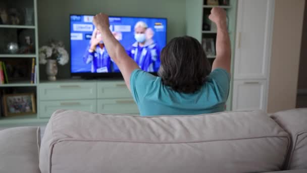 Dorosły mężczyzna ogląda telewizję, rywalizuje i wiwatuje za swój kraj.. — Wideo stockowe