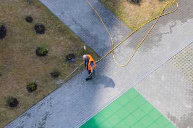 Bir işçi sıcak güneşin hortumuyla bahçedeki çalıları suluyor..