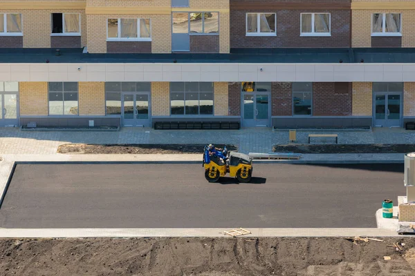 Workers of special equipment are laying asphalt near a house under construction. — Stock Photo, Image