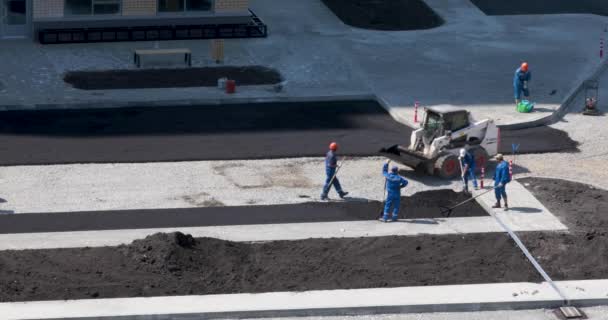 Eine Gruppe Arbeiter ebnet losen Asphalt für die Verdichtung mit einer Walze — Stockvideo