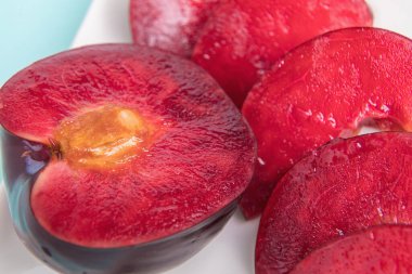 Beyaz bir tabakta, büyük bir erik, ortadan ikiye bölünmüş, yanında da dilimler var. Kırmızı böğürtlen posası. Yakın plan..