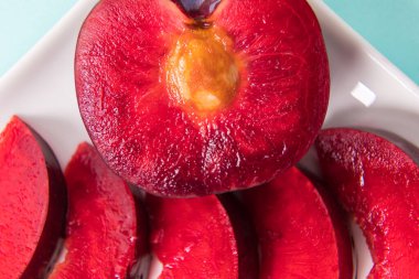 Beyaz bir tabakta, büyük bir erik, ortadan ikiye bölünmüş, yanında da dilimler var. Kırmızı böğürtlen posası. Yakın plan..