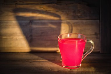 Kırmızı jöleli cam bardak. Bardaktan büyük bir gölge tahtadan duvara yansıtılıyor..