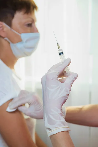 A girl doctor in white gloves makes a vaccination, a vaccine against coronavirus, flu. — Stock Photo, Image