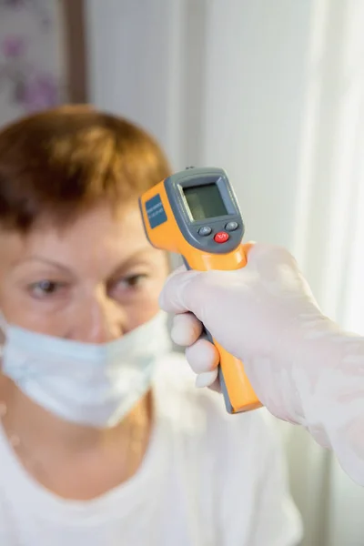 Lékařka měří teplotu dospělé ženy pomocí laserového zařízení. — Stock fotografie