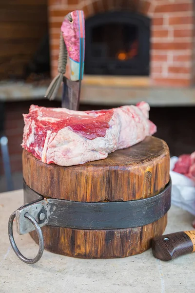 Raw meat on a deck, a knife stuck in the meat. Fresh meat on a cutting board. Close-up.