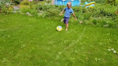 Yeşil çimlerde futbol oynayan bir çocuk. Çocuk çimenlerde yalın ayak koşar ve topa vurur..