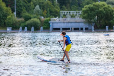 Bir çocuk sörf tahtasının üzerinde yüzüyor, kürekle itiyor. Paddleboard.