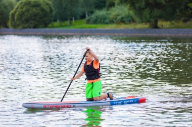 Bir çocuk sörf tahtasının üzerinde yüzüyor, kürekle itiyor. Paddleboard.