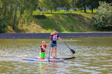 Bir çocuk sörf tahtasının üzerinde yüzüyor, kürekle itiyor. Paddleboard.