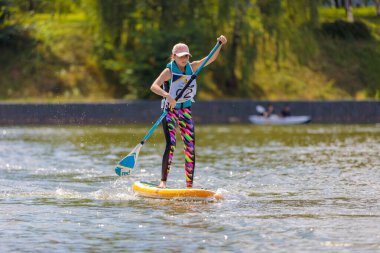 Bir çocuk sörf tahtasının üzerinde yüzüyor, kürekle itiyor. Paddleboard.